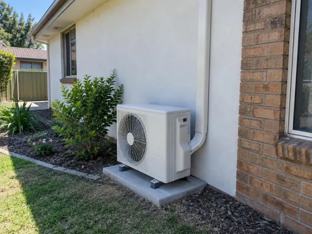 Outdoor air conditioner unit on a concrete pad beside a brick home and garden in Salisbury Downs